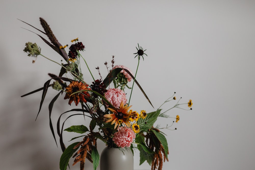 verschiedene Blumen in der Vase neben der Wand