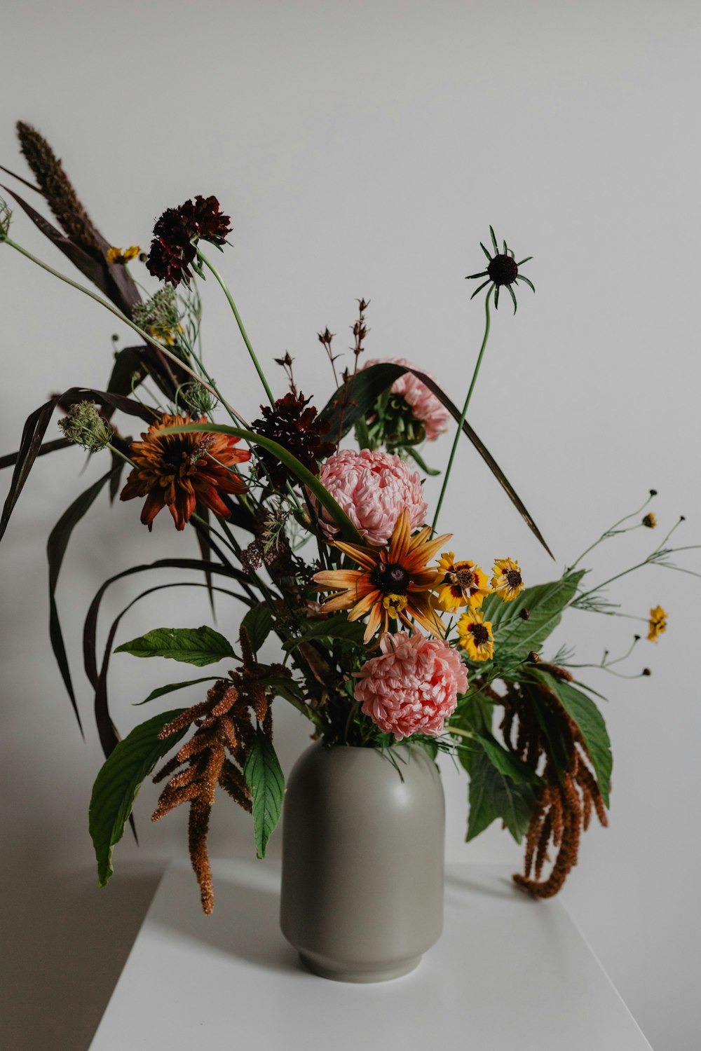 yellow and pink flowers in grey vase on white surface