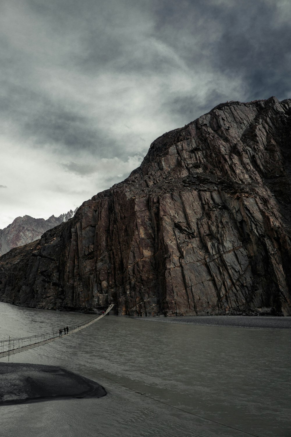 bridge above water towers rock mountain under cloudy sky