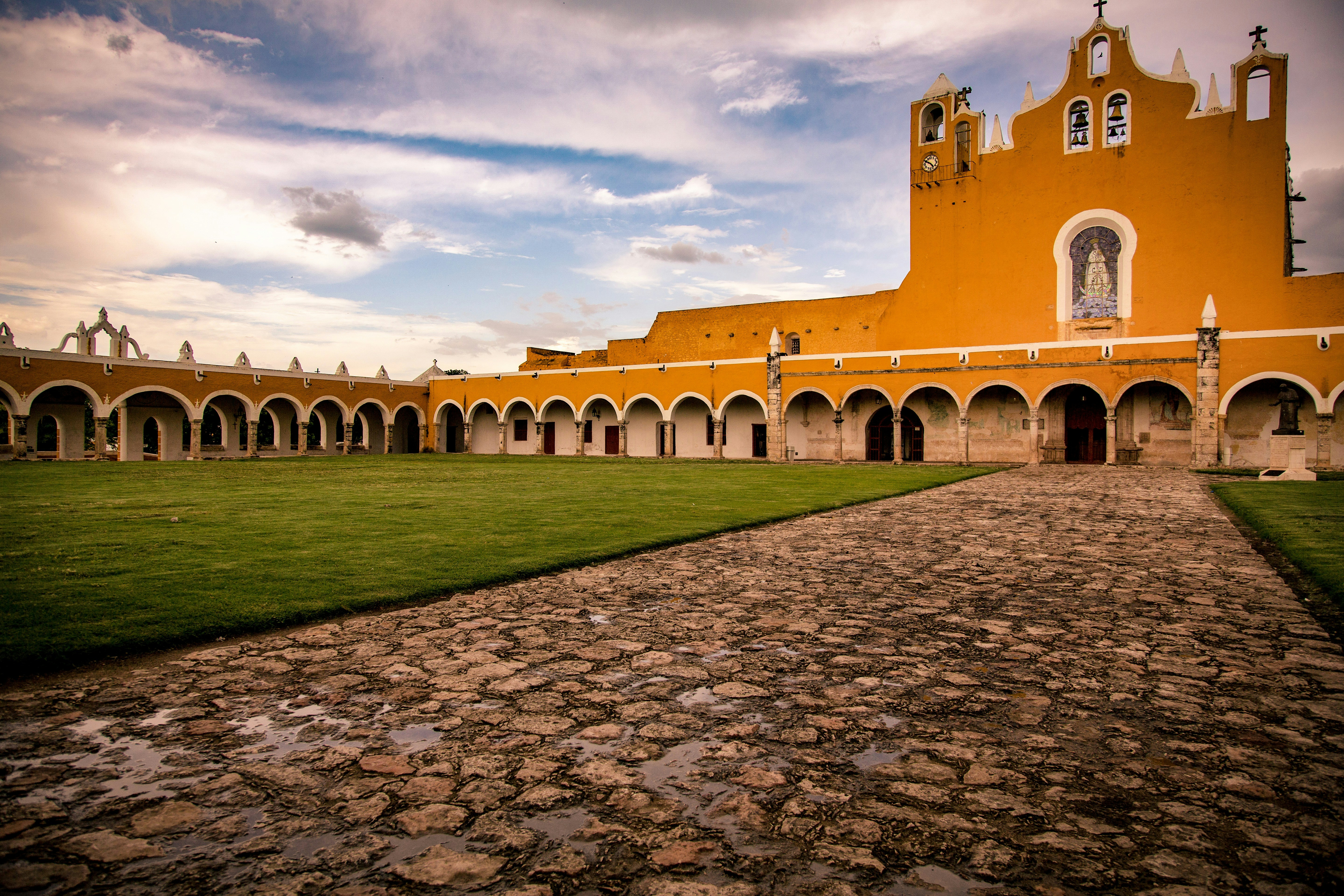 church near grass and pathway during day, Yellow cloister in monastery on a cloudy afternoon.