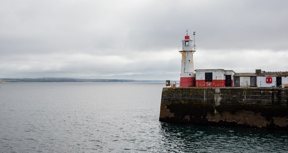 white and red lighthouse on brown rock formation near sea under white clouds during daytime