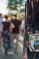 A close-up of colorful, owl-themed bags with straps hanging in the foreground, with a blurred background showing people walking outdoors.