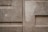 A textured concrete wall featuring rectangular patterns and subtle variations in color. The surface appears worn and slightly uneven with visible lines and angular shapes.