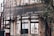 An exterior view of a partially renovated building with an old, weathered facade. A large banner hangs above with a message in Portuguese about renovating the neighborhood. The building's walls show signs of decay, with visible scaffolding and an urban setting surrounding it. A tree is seen to the right of the image.