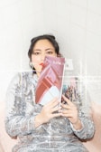 A person wearing a sequined dress leans against a tiled wall and holds a magazine titled 'Bob Cut' covering part of their face. The image has a sparkling, glittery effect overlay.