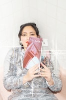A person wearing a sequined dress leans against a tiled wall and holds a magazine titled 'Bob Cut' covering part of their face. The image has a sparkling, glittery effect overlay.