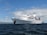 A large white cruise ship named Galapagos Legend is anchored on a calm ocean with a clear blue sky and scattered clouds. The ship features multiple decks and a prominent funnel, indicating it is well-equipped for luxury travel.
