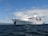 A large white cruise ship named Galapagos Legend is anchored on a calm ocean with a clear blue sky and scattered clouds. The ship features multiple decks and a prominent funnel, indicating it is well-equipped for luxury travel.
