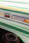 A close-up of a vintage vehicle's side featuring the brand insignia 'FORD 250'. The panel is decorated with green and yellow stripes. A signal light is mounted next to the badge, and part of a weathered wheel is visible below.