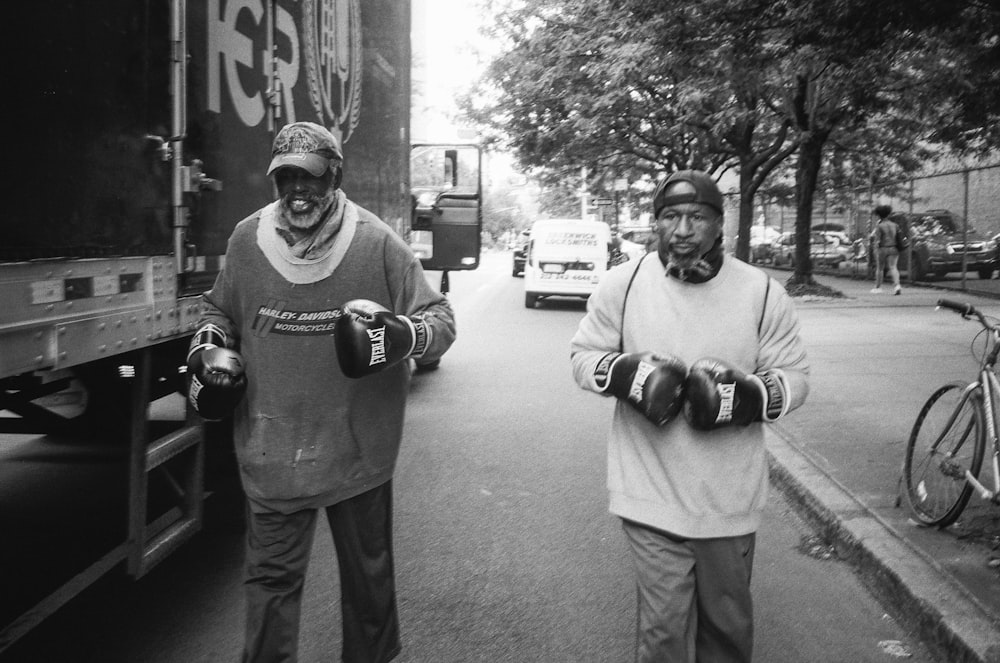 two men wearing boxing gloves walking at the side of the road beside truck
