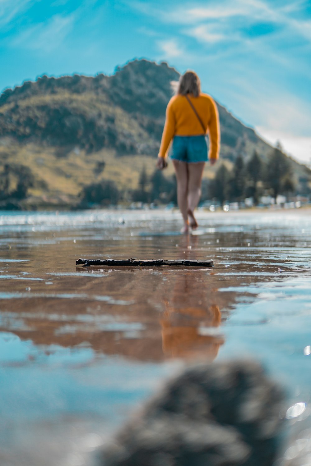 barefooted woman walking near seashore under blue and white skies during daytime