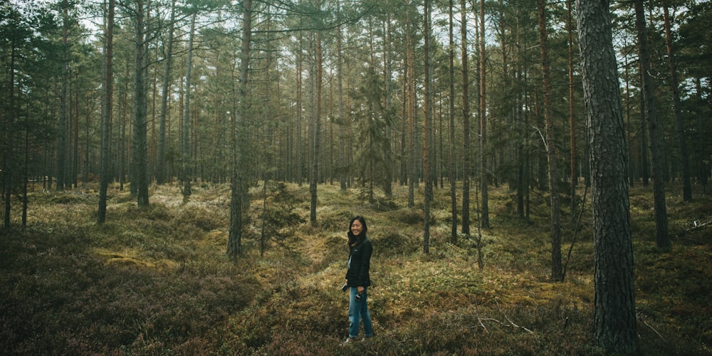 woman standing surrounded with tall and green trees