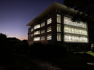 A contemporary building facade showcasing glass, concrete, and landscaped surroundings at dusk.