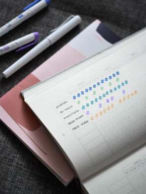 Close-up of a colorful habit tracker journal open on a wooden desk with a pen resting on it.