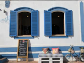two multicolored throw pillows on bench near bike parking on white and blue wall showing open blue wooden windows