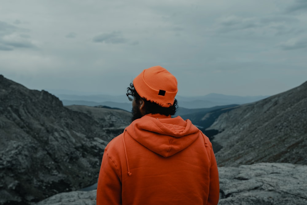 person in orange cap and jacket by mountain slopes