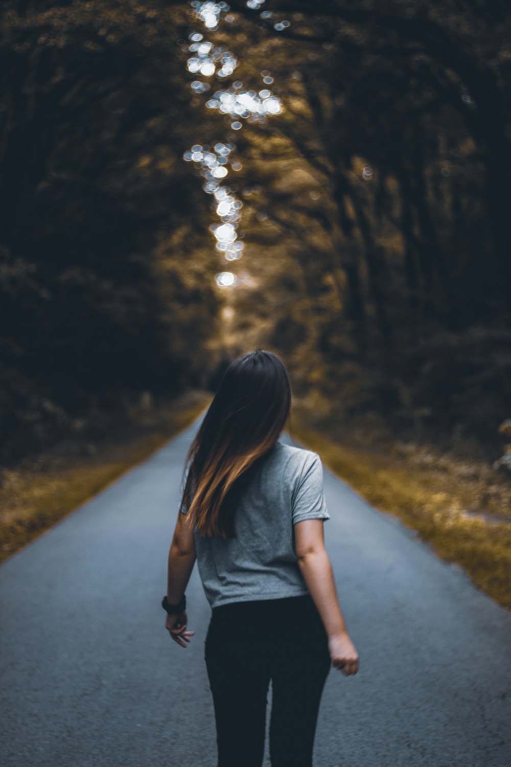 woman walking on empty road between trees
