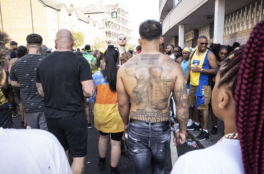 topless man showing back tattoo walking within crowd