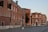 A square in Italy with historic buildings featuring ornate architectural details. The warm-colored facades of the buildings are bathed in the soft light of late afternoon, with a clear sky above. A couple of lampposts and some greenery add charm to the scene.