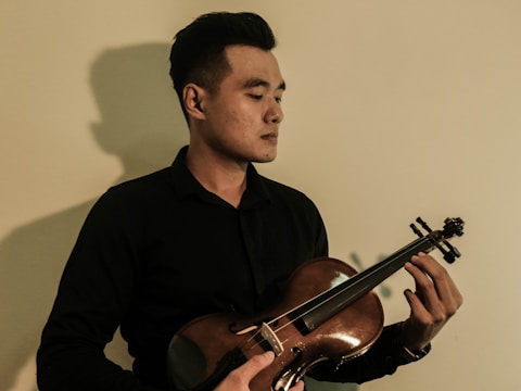 Portrait of musician in black attire holding a violin against a white backdrop