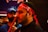 The image shows a close-up of a man wearing a red headband with white script. His expression is calm and focused. In the background, another person in a blue shirt and cap is visible, slightly out of focus.