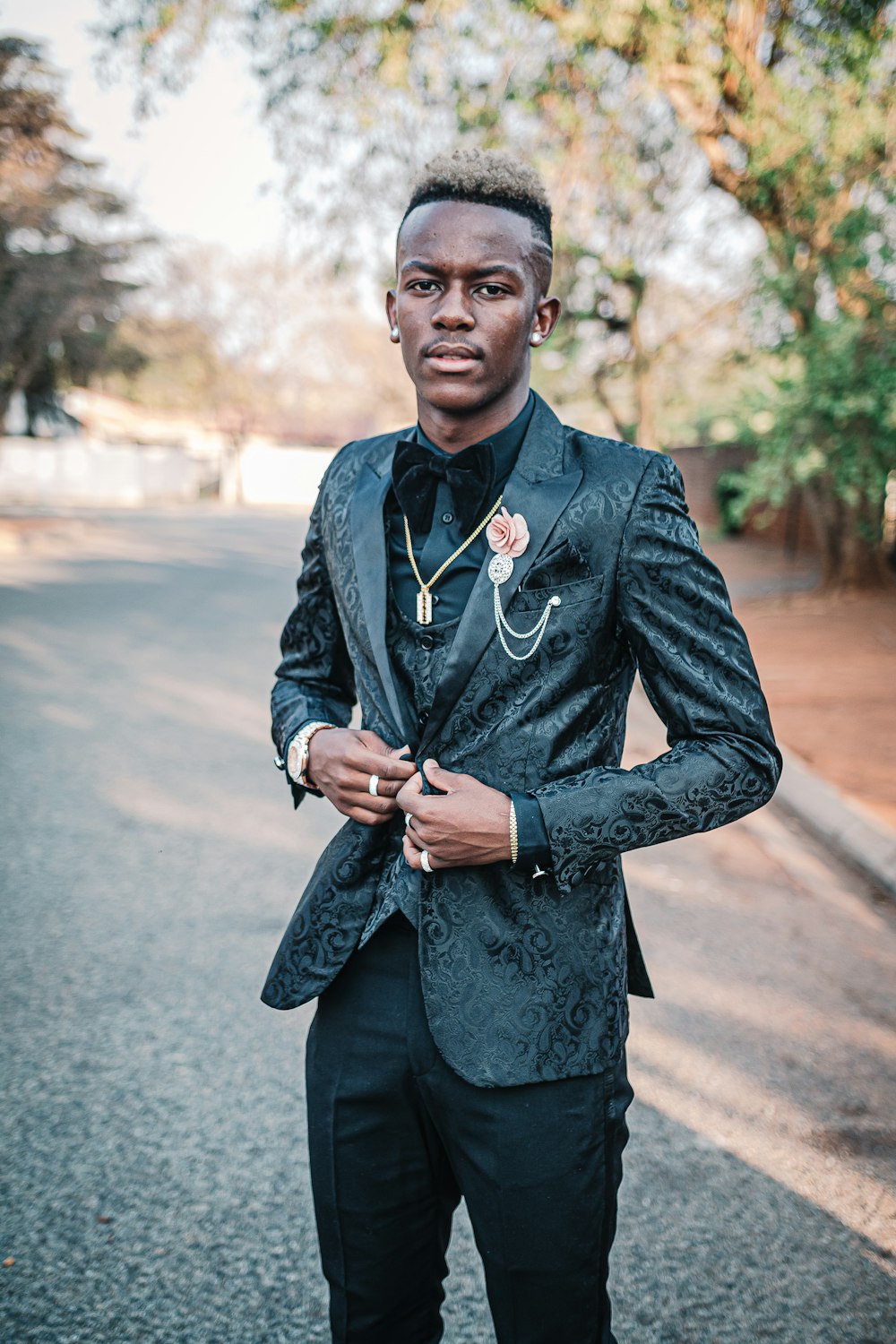 man wearing black notched lapel suit jacket standing on concrete pathway