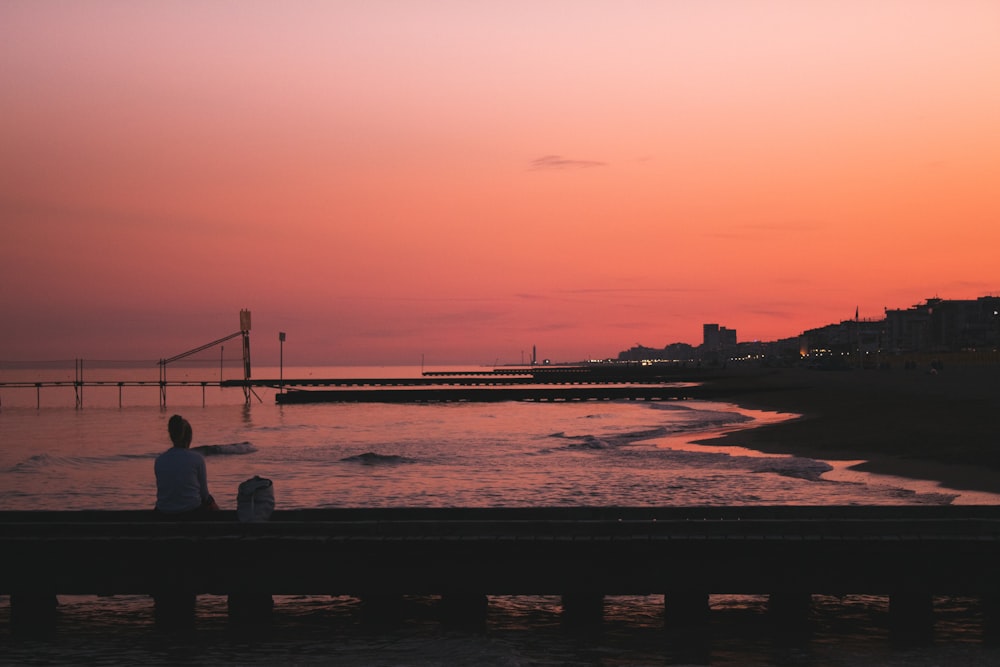 silhouette photo of woman sitting on bridge