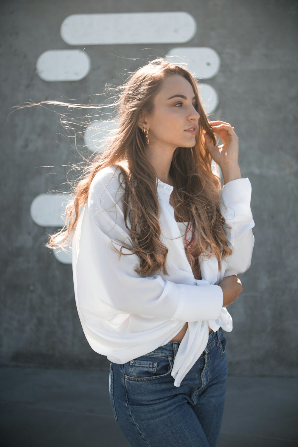 woman in white top and blue denim bottoms standing outdoors