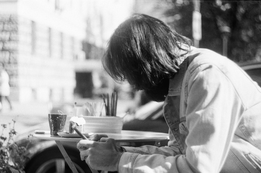 grayscale photography of person using phone while sitting near table