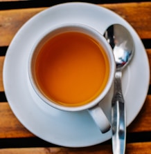 An inviting glass of bright orange juice beside a steaming cup of tea on a cozy wooden table.