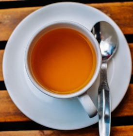 An inviting glass of bright orange juice beside a steaming cup of tea on a cozy wooden table.