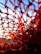 A close-up view of a red netting material, with intricate threads forming a web-like pattern. The background features a gradient of blue sky and a bright sunlight is visible through the woven structure.