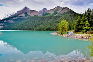 A group of trekkers resting beside a crystal-clear lake near Senaru, surrounded by lush green forest.