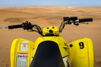 Close-up of a rider gripping the handlebars of a quad bike with desert dunes stretching behind.