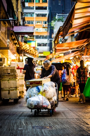 A smiling caregiver helping an elderly person with shopping bags in a bright, outdoor setting.