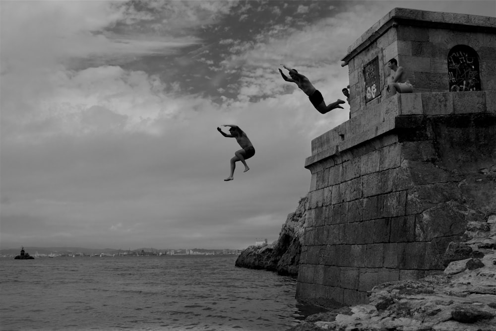 two men dive into the sea water from concrete building