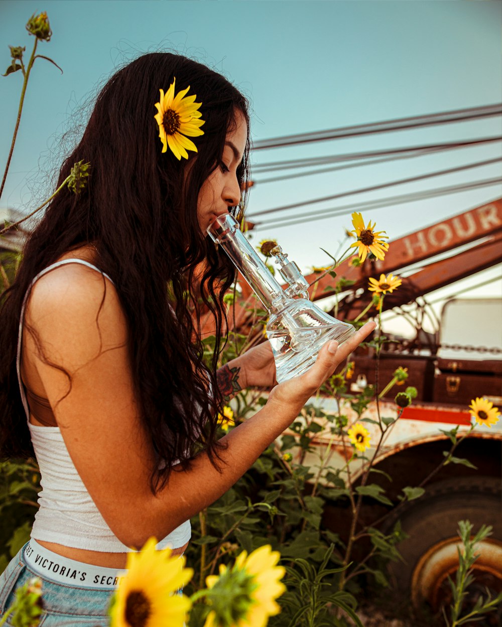 woman holding glass water bong while standing near yellow sunflower