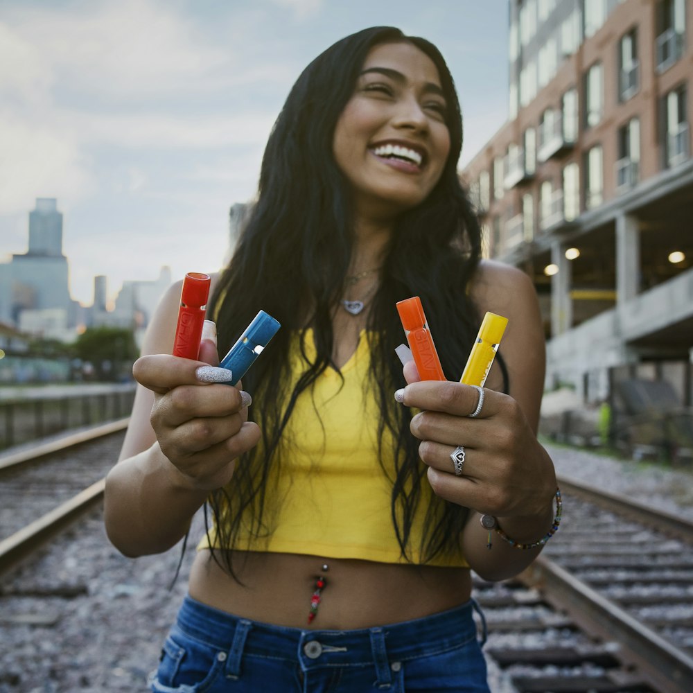 Mujer sonriente sosteniendo botellas de colores variados mientras está de pie en los rieles del tren