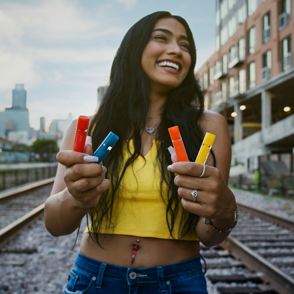 smiling woman holding assorted-color bottles while standing on train rails