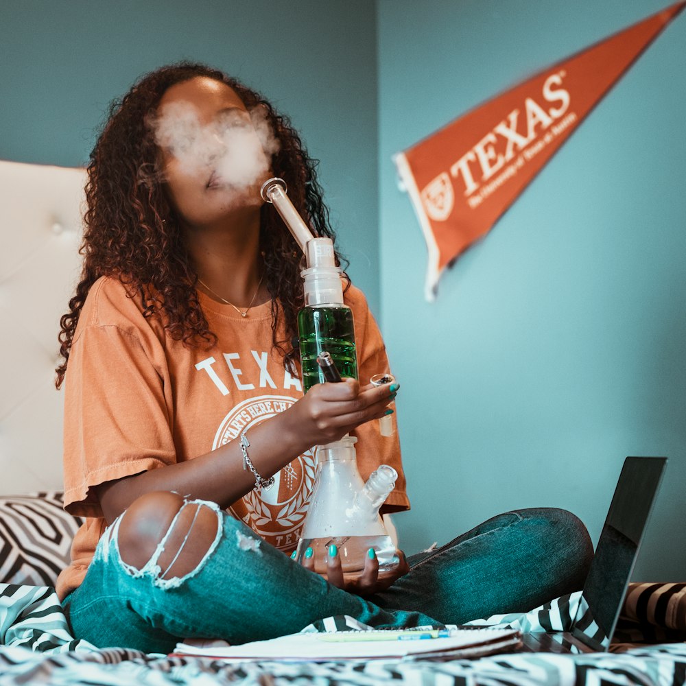 woman holding glass water bong while sitting on bed