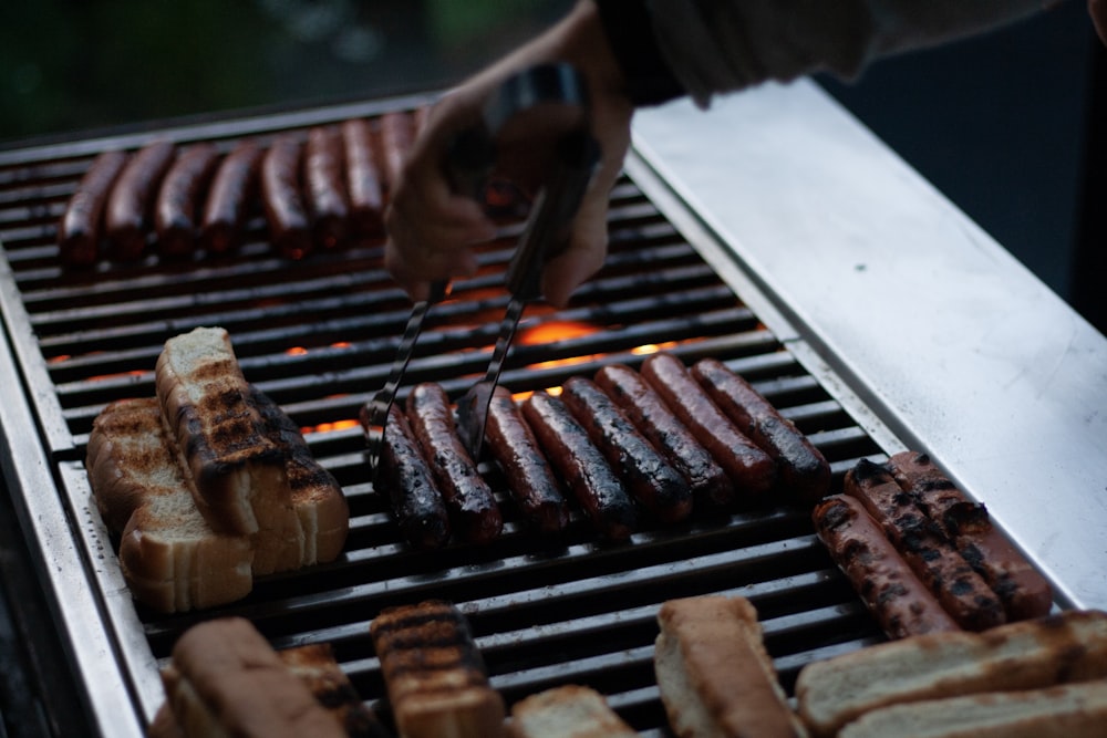 person flipping hotdogs on grill