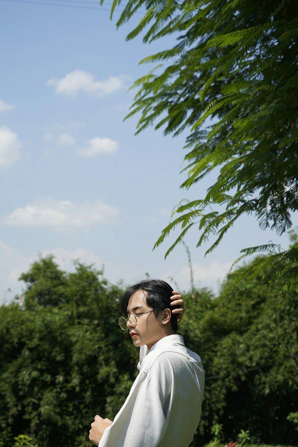 standing man wearing gray framed eyeglasses beside trees during daytime