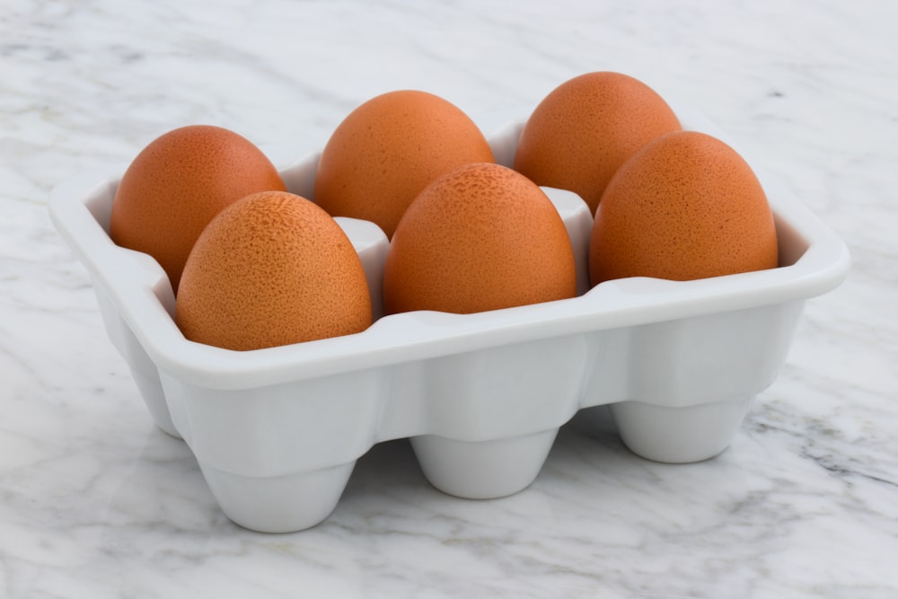 Sechs braune Eier auf weißem Tablett