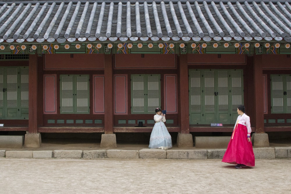 two women wearing Hanbok dresses standing in front of building