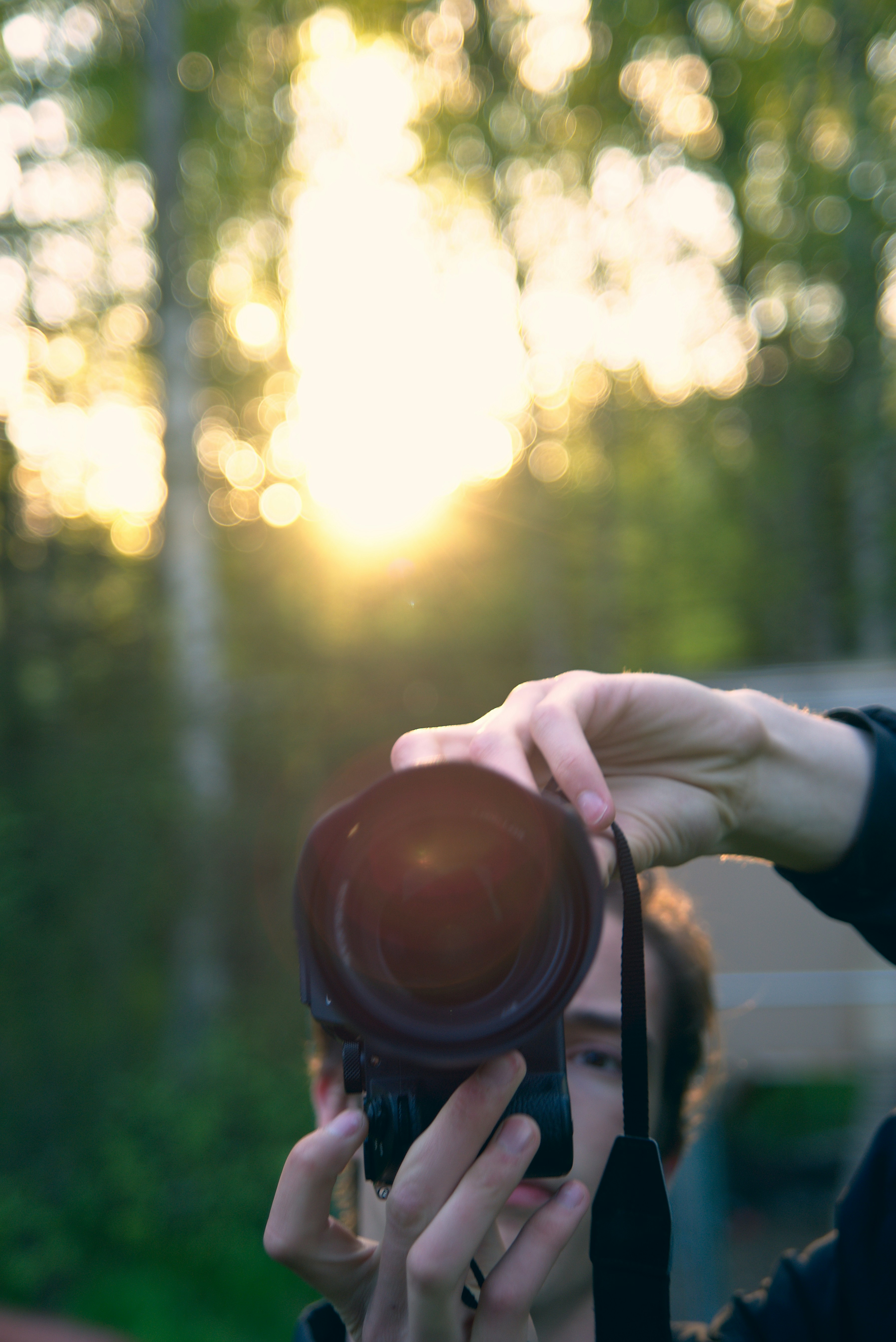 Professional photographer holding vintage camera with warm smile in natural outdoor setting with golden hour lighting