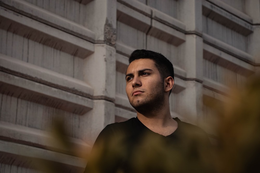 man wearing black shirt leaning on white wall