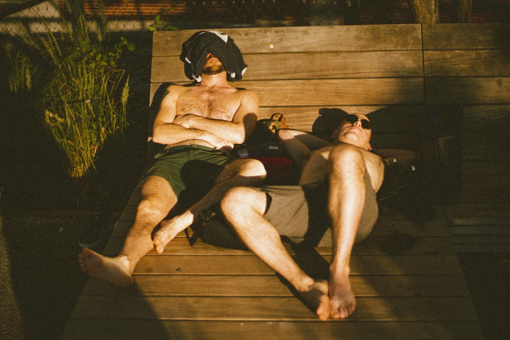 two topless men sleeping on wooden pavement