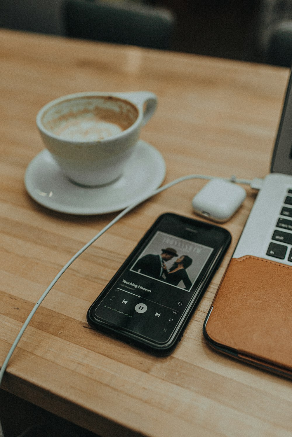 iPhone beside MacBook and cup of coffee on table