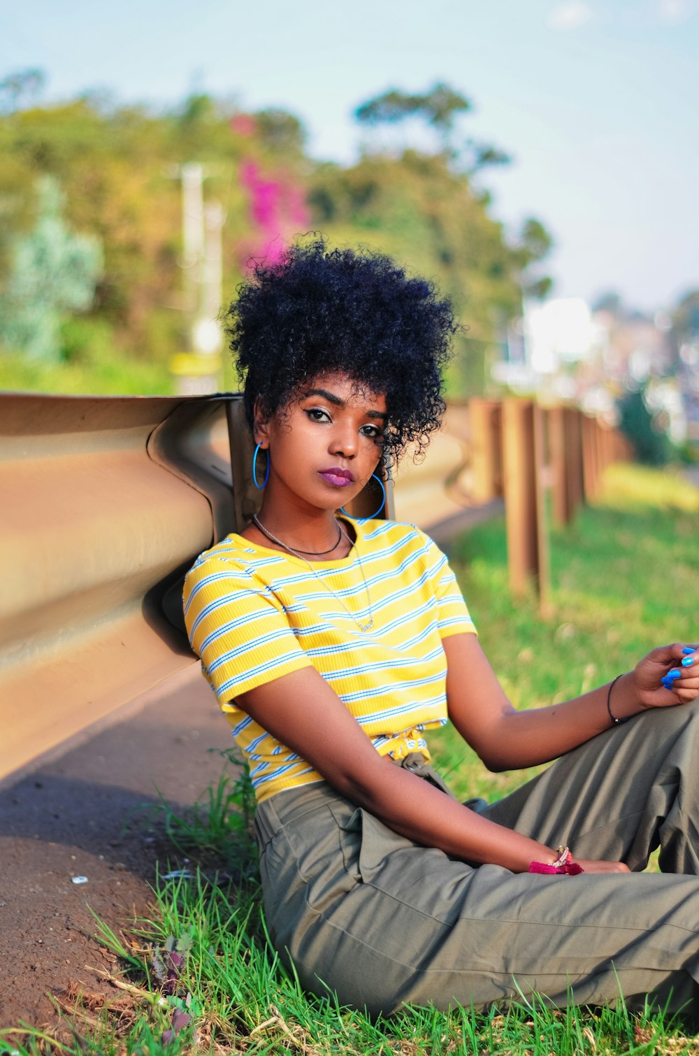 woman sitting on grass while leaning on road guardrail