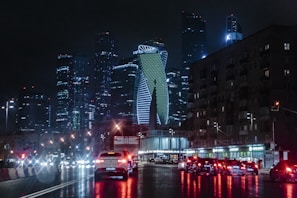 different vehicles on road viewing city with high-rise building during night time